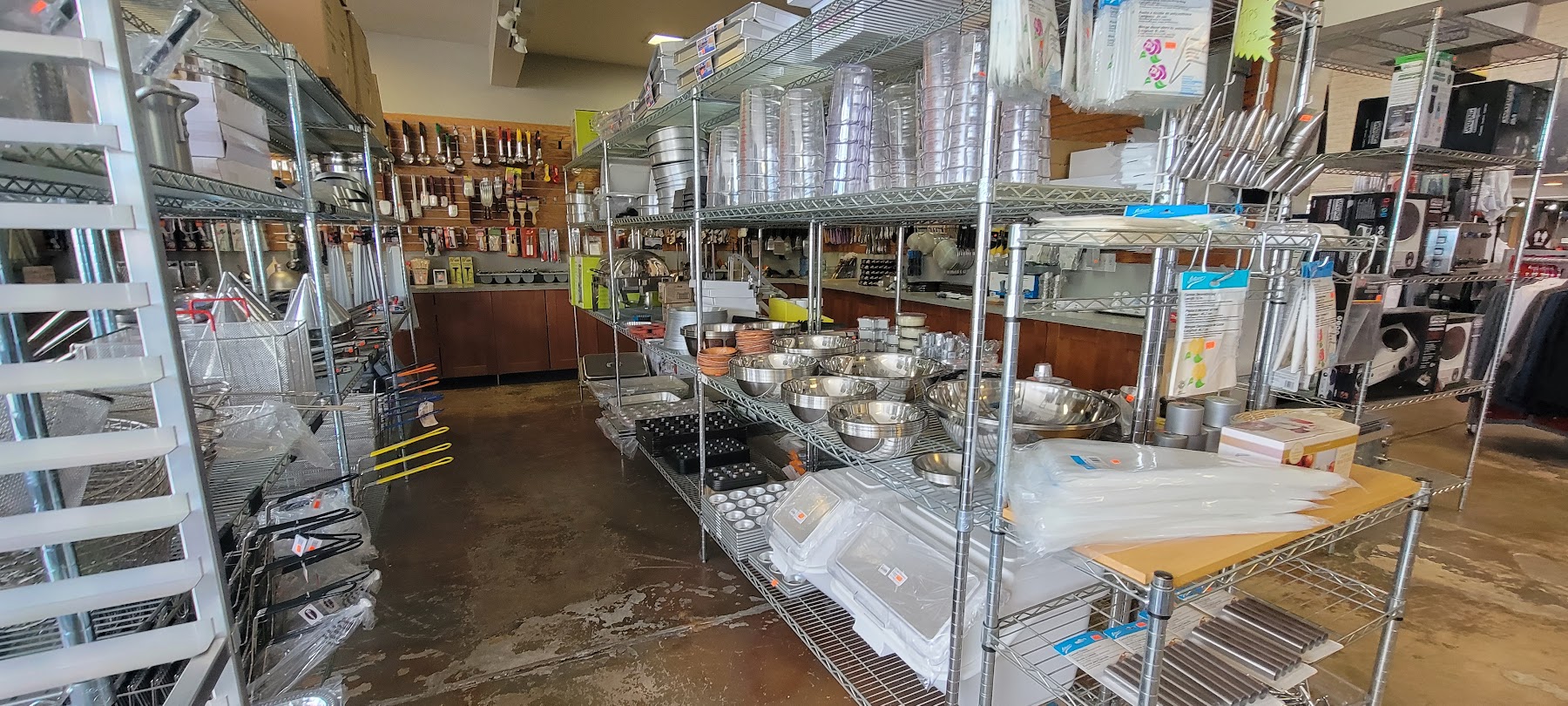 The Knife Guys shop floor in Denver with metal kitchen-supply racks, knives, bowls, tools, and restaurant equipment.